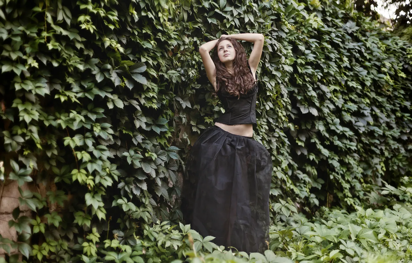 Фото обои девушка, стена, растения, брюнетка, стоит, в чёрном, позирует