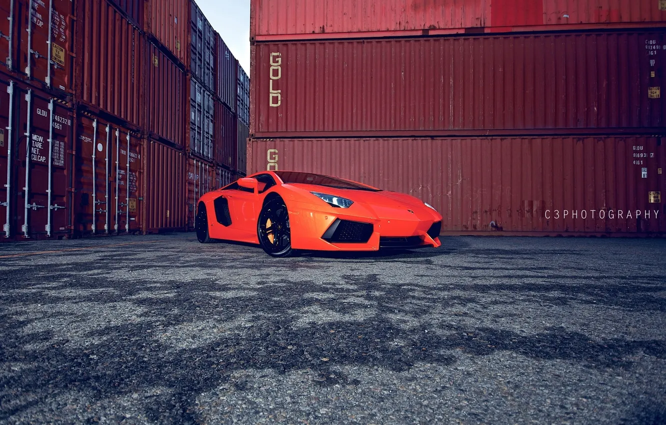 Фото обои оранжевый, lamborghini, вид сбоку, мокрый асфальт, контейнеры, orange, свет фар, aventador